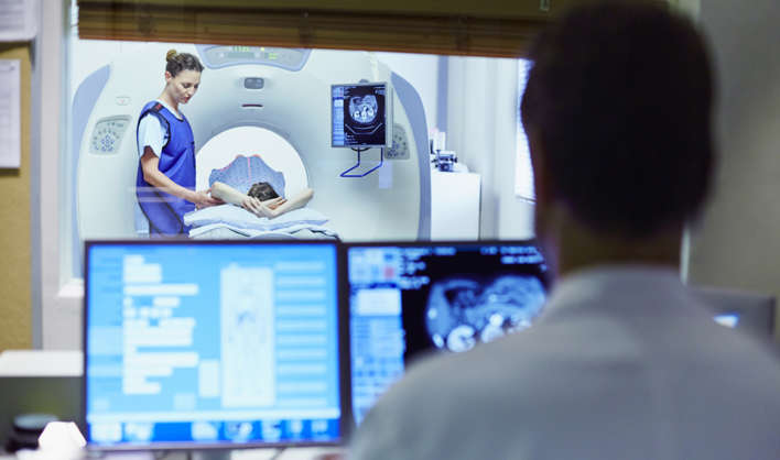 View of doctor preparing patient for CT scan from control room at hospital